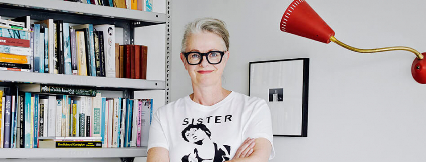 The workshop tutor, a woman, at home against a bookshelf.