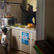 A child actor standing in a kitchen with three crew members watching.
