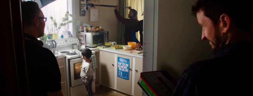 A child actor standing in a kitchen with three crew members watching.